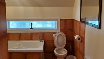 A bathroom with a bathtub, toilet, and a window above the sink.