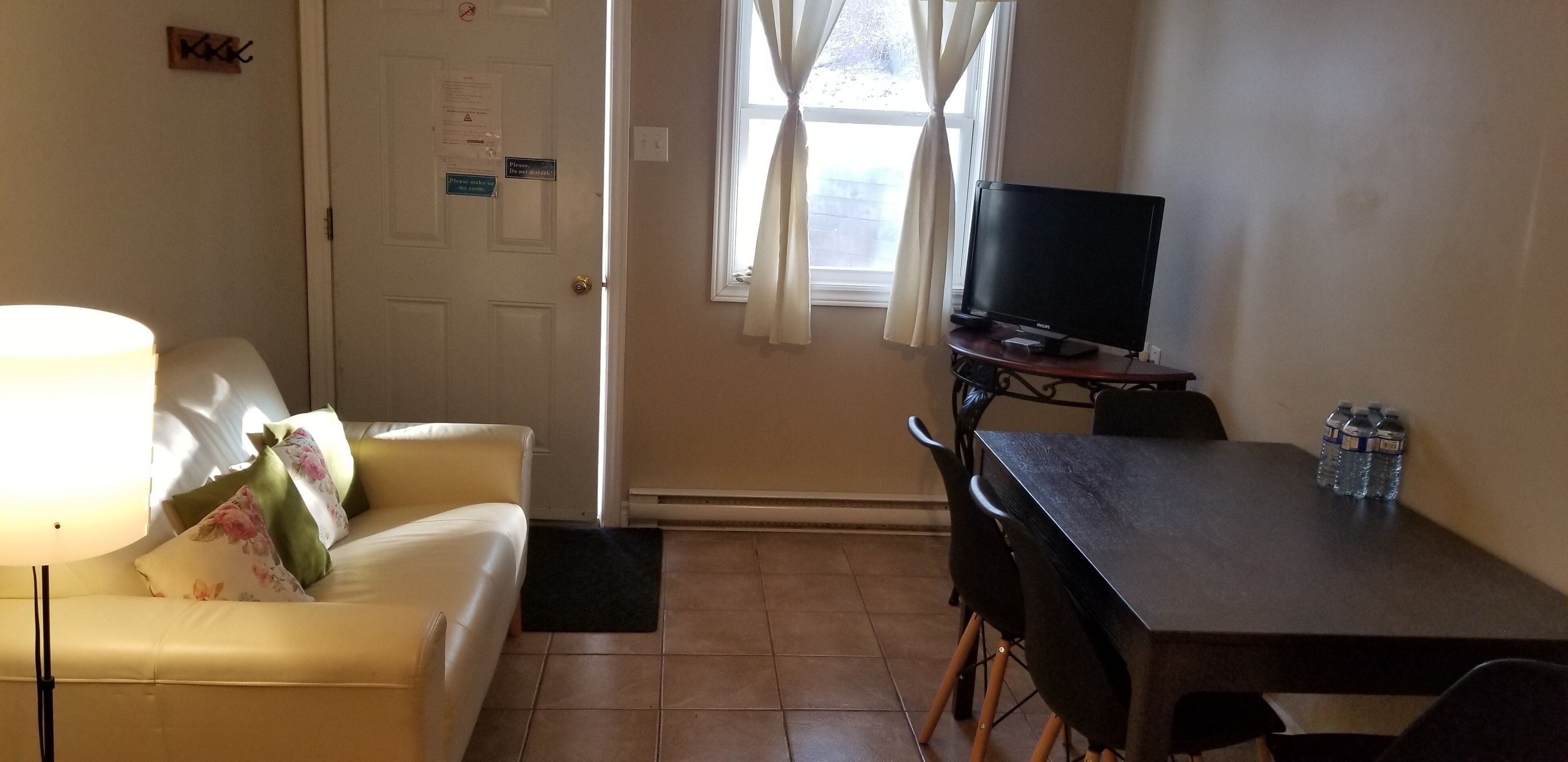 A room with a yellow sofa, a black TV on a stand, a dining table with chairs, and a window with curtains.