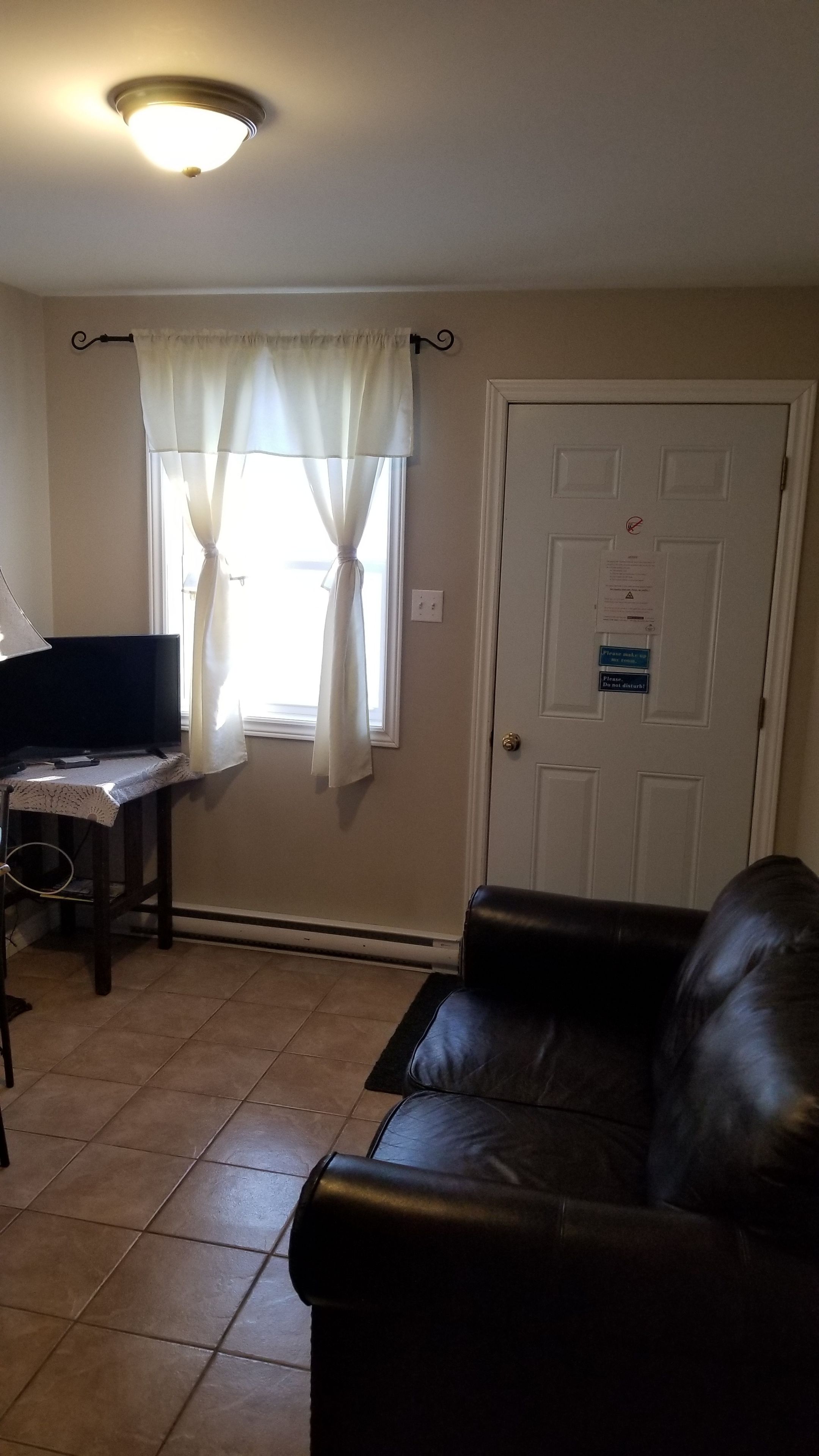 A living room with a leather couch, a television on a stand, a window with curtains, and a door with a sign.