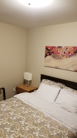 A hotel room with a bed, a nightstand, a lamp, and a painting on the wall. - Rothesay Motel (Rothesay)