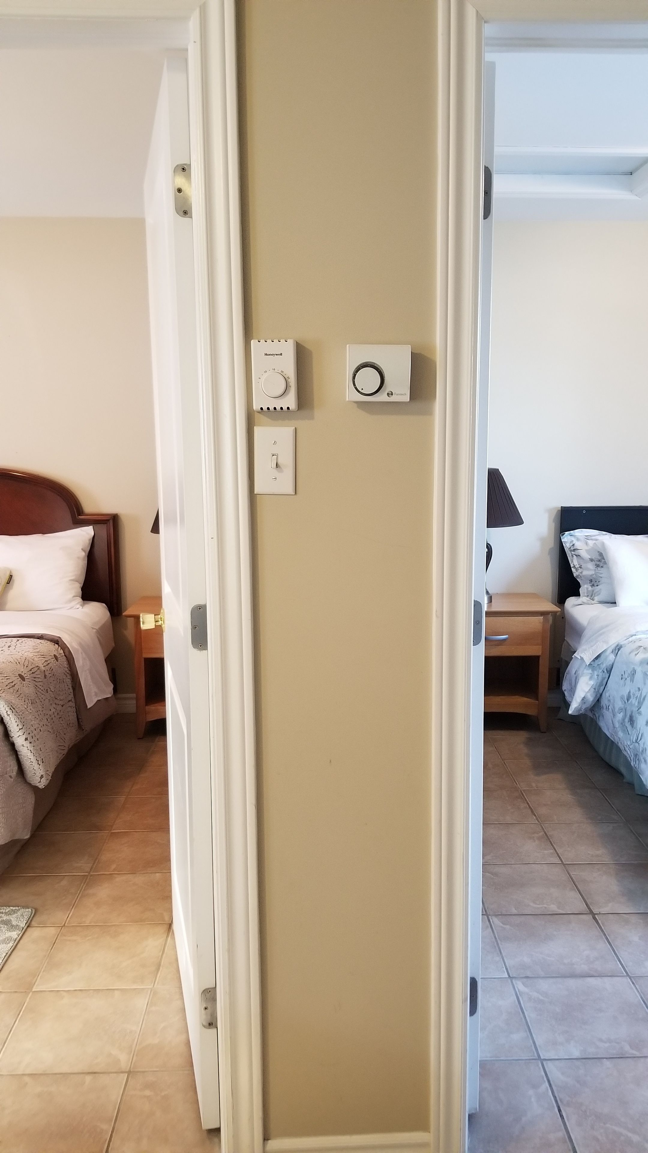 Ett hotellrum med en säng, ett sängbord och en termostat på väggen.