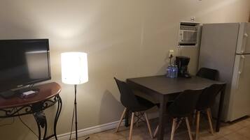 Uma cozinha compacta com mesa, cadeiras, televisão, luminária, cafeteira e geladeira.