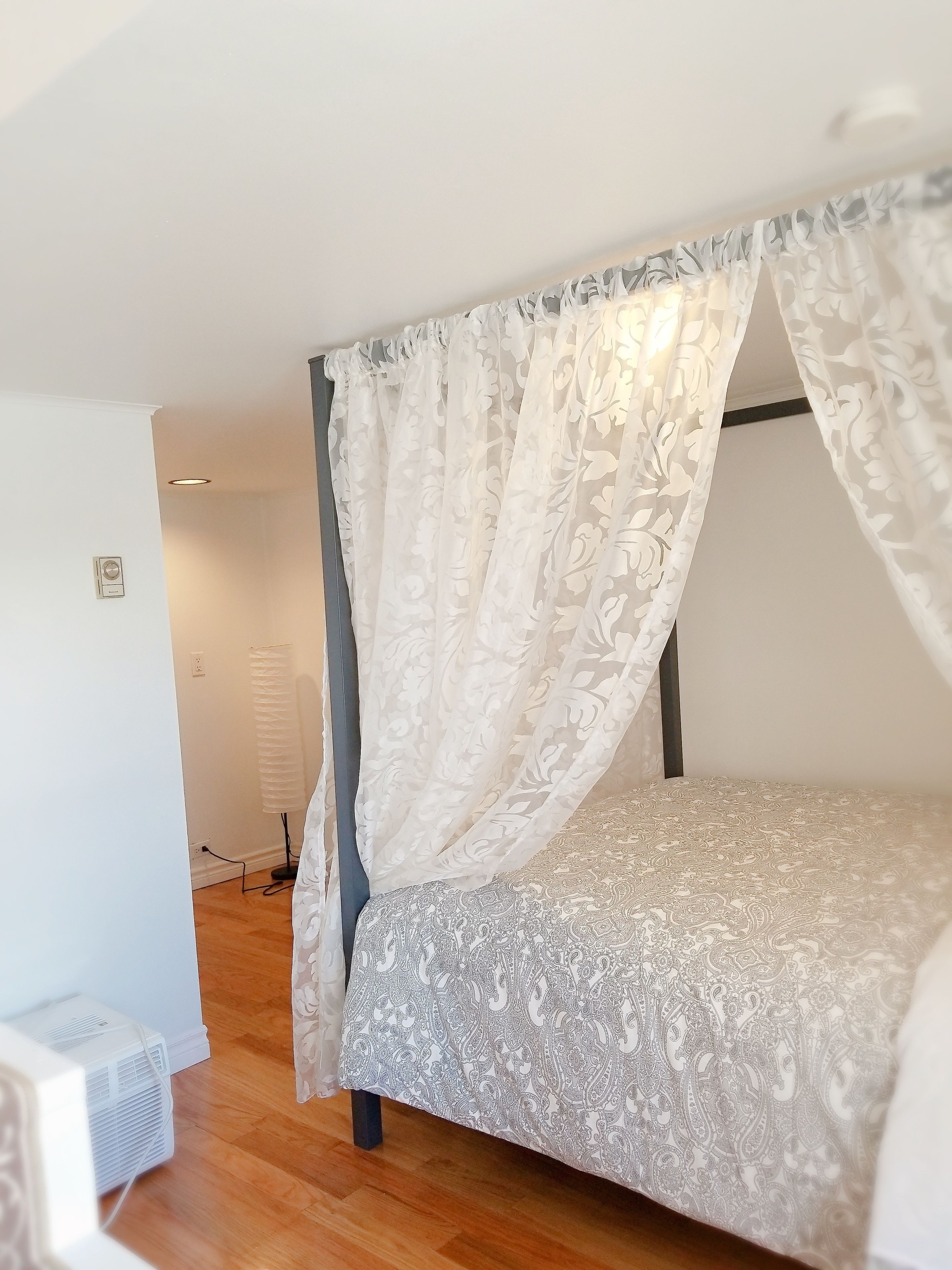 Un dormitorio con cama con dosel, un calentador portátil y un aire acondicionado blanco.