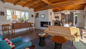A spacious living area with a high wooden ceiling, a fireplace, a sofa, a coffee table, and a dining area with a chandelier. - Rare Find: Home + Private Casita | Pool & Spa (Palm Springs)