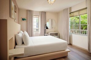 A modern bedroom with a large bed, a bedside table, a round mirror, and a window with curtains.