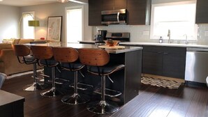 A modern kitchen with dark cabinetry, stainless steel appliances, and a central island with bar stools. - Walking distance to downtown Elk Rapids, Elk Lake and dining (Elk Rapids)