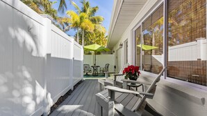 Une terrasse avec une clôture blanche, des meubles d’extérieur et une vue sur des palmiers.