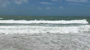 Une plage où les vagues se brisent sur le rivage, un ciel dégagé et un horizon lointain.