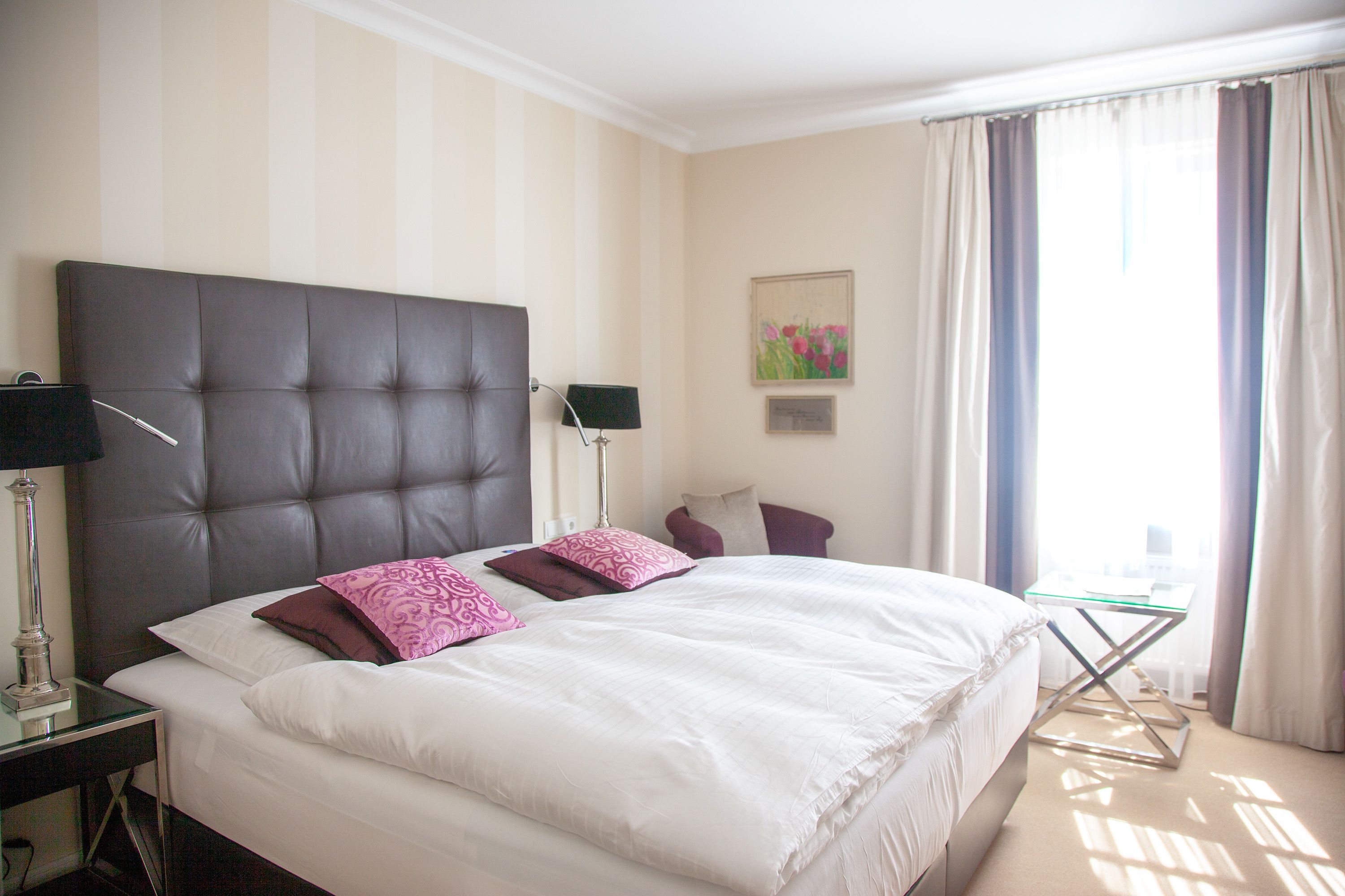A hotel room with a large bed, two bedside tables with lamps, a small desk, and a window with curtains.