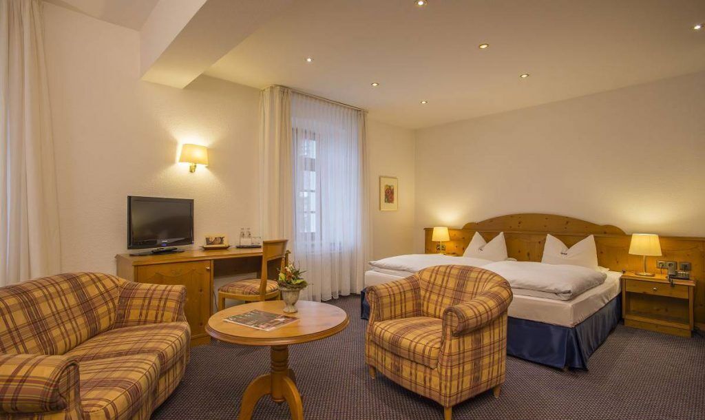 Une chambre d’hôtel comprenant un lit, deux fauteuils, un canapé, une télévision, un bureau et une lampe.