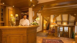 A chef at a wooden bar counter in a warmly lit kitchen with a rustic interior, a staircase, and a view of a door leading outside. - Landhotel Donner (Meschede)
