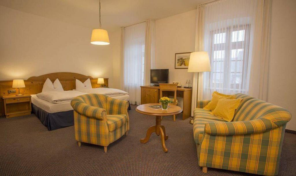 Ein Hotelzimmer mit einem Bett, zwei Sesseln, einem kleinen Tisch, einem Fernseher und einer Lampe.
