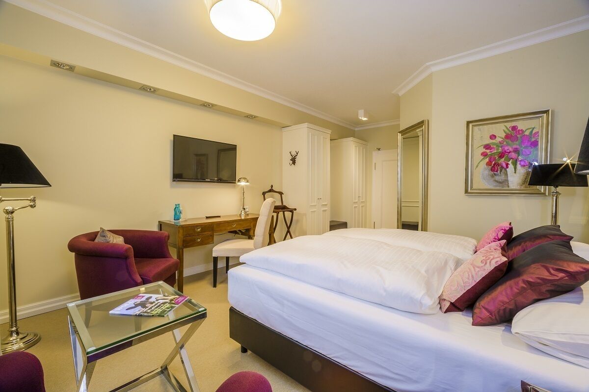 Quarto de hotel com cama, escrivaninha, cadeira, televisão e um quadro na parede.