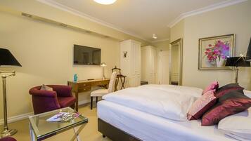 Quarto de hotel com cama, escrivaninha, cadeira, televisão e um quadro na parede.