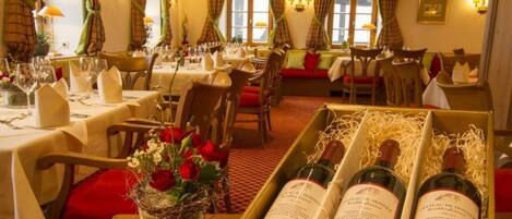A restaurant with tables set for dining, a basket of flowers, and bottles of wine on a table.