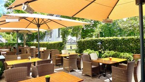 An outdoor patio area with wicker furniture and yellow umbrellas. - Landhotel Donner (Meschede)