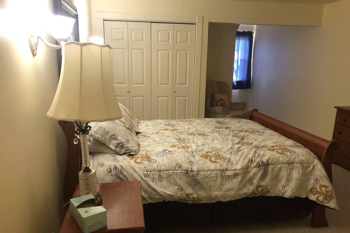 A bedroom with a bed, a nightstand, a lamp, a dresser, and a door.