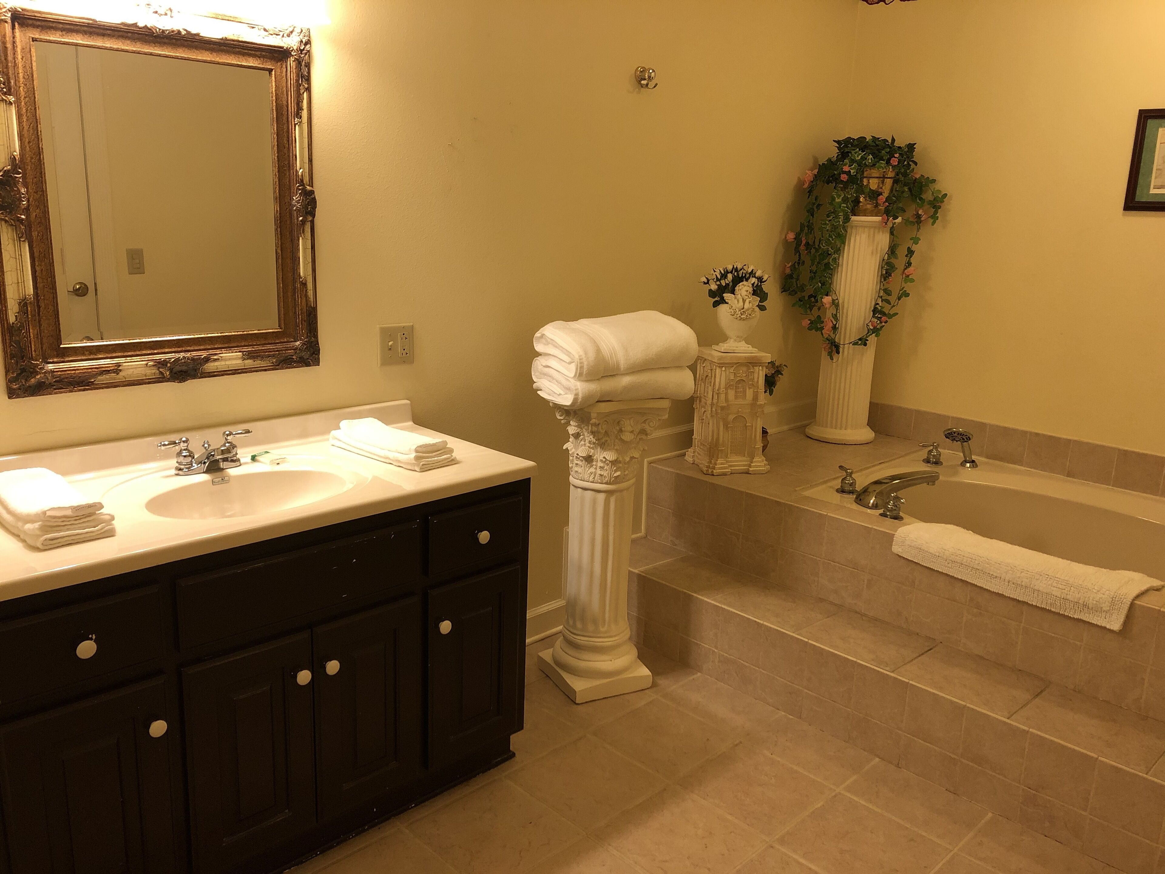 Un baño con tocador de doble lavabo, un espejo grande, una bañera y plantas decorativas.