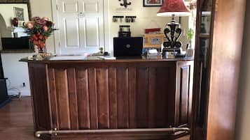 A wooden reception desk with a laptop, a red lamp, and a vase of flowers.