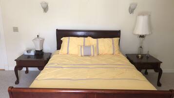 A neatly made bed with a wooden headboard, two bedside tables with lamps, and a plain wall with a light switch.