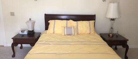 A neatly made bed with a wooden headboard, two bedside tables with lamps, and a plain wall with a light switch.