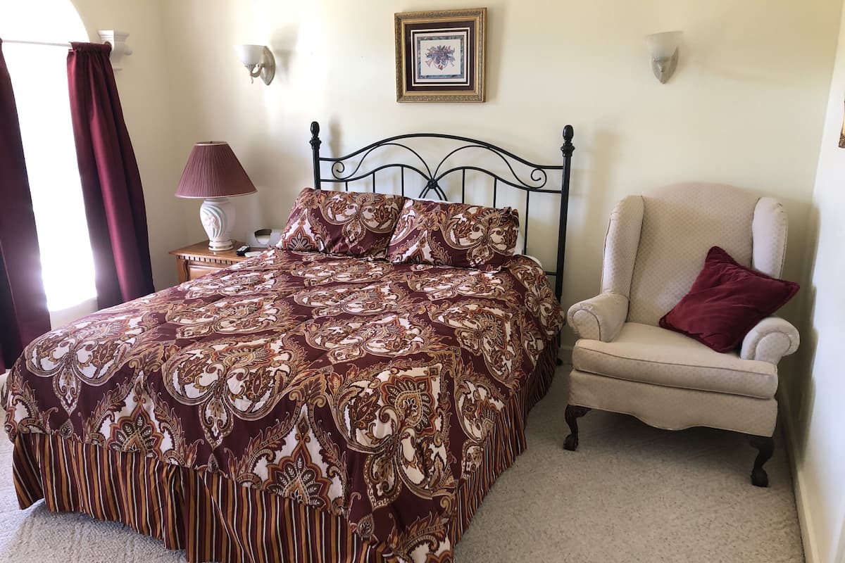 A bedroom with a large bed, a chair, a lamp, and a framed picture on the wall.
