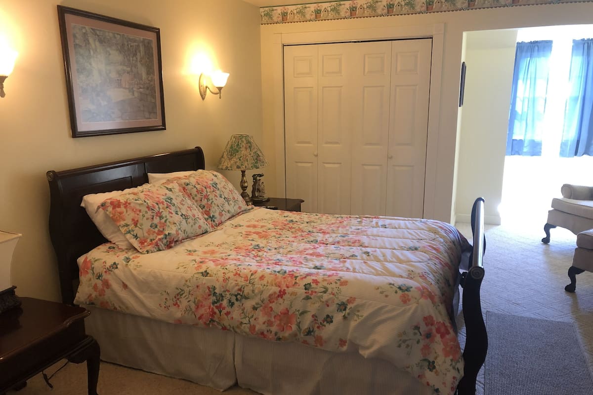 A bedroom with a bed, a nightstand, a lamp, a door, and a chair.