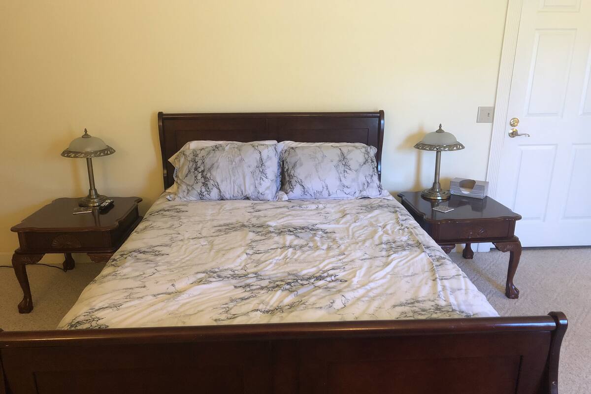 A bed with a marble-patterned bedspread, two bedside tables with lamps, and a door in the background.