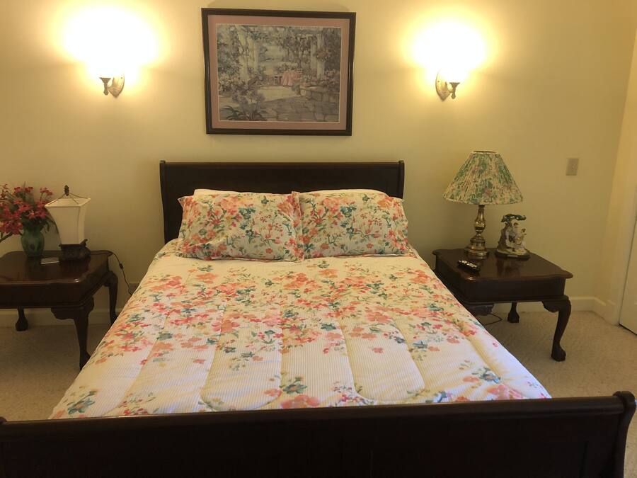Une chambre à coucher avec un lit, deux tables de chevet, une lampe, un vase de fleurs et un tableau encadré accroché au mur.