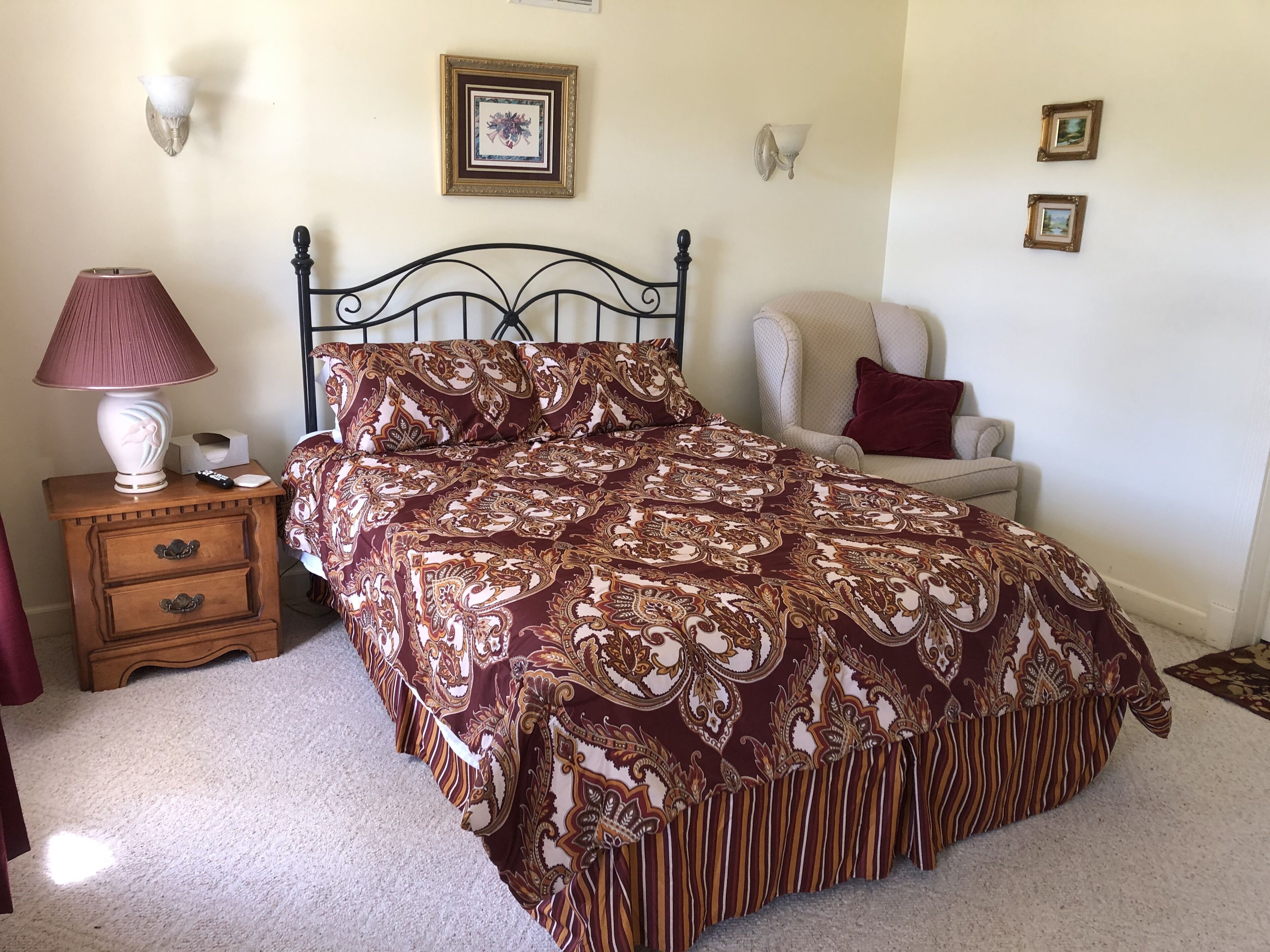 A bedroom with a bed, a nightstand, a lamp, and a chair.