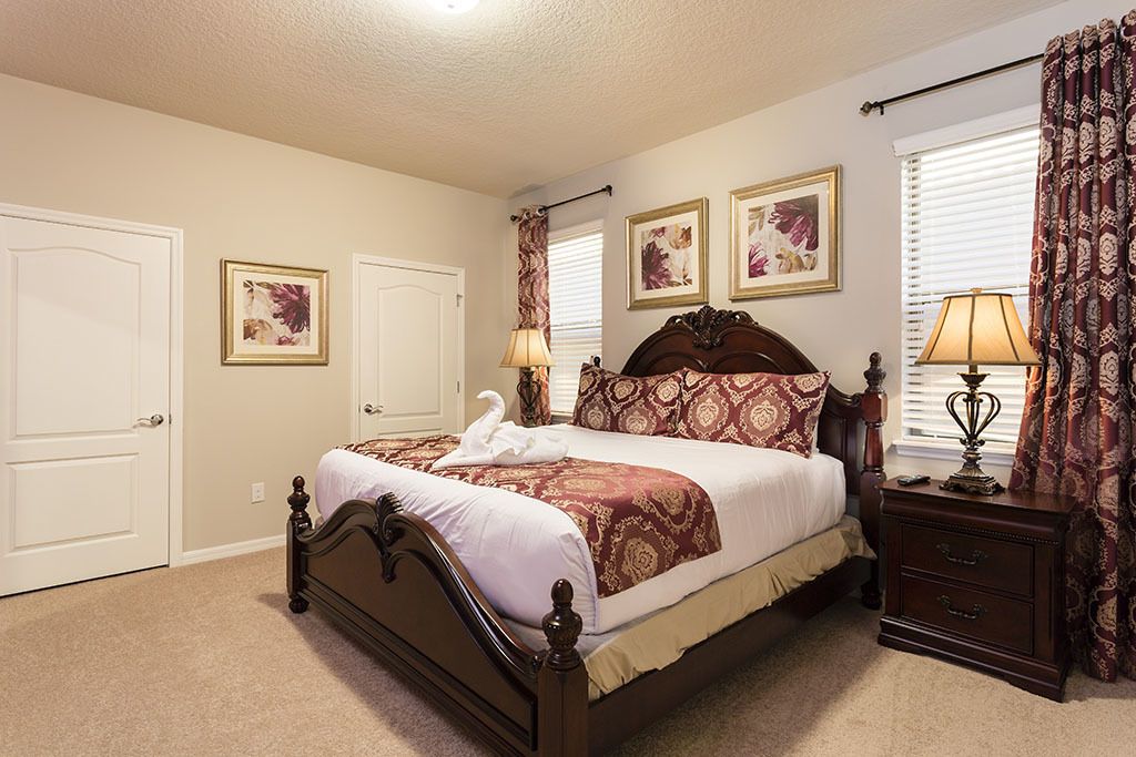 A bedroom with a large bed, two bedside tables, a nightstand, and a window with curtains.