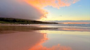 A beach with a calm sea, a clear sky, and a sunset.