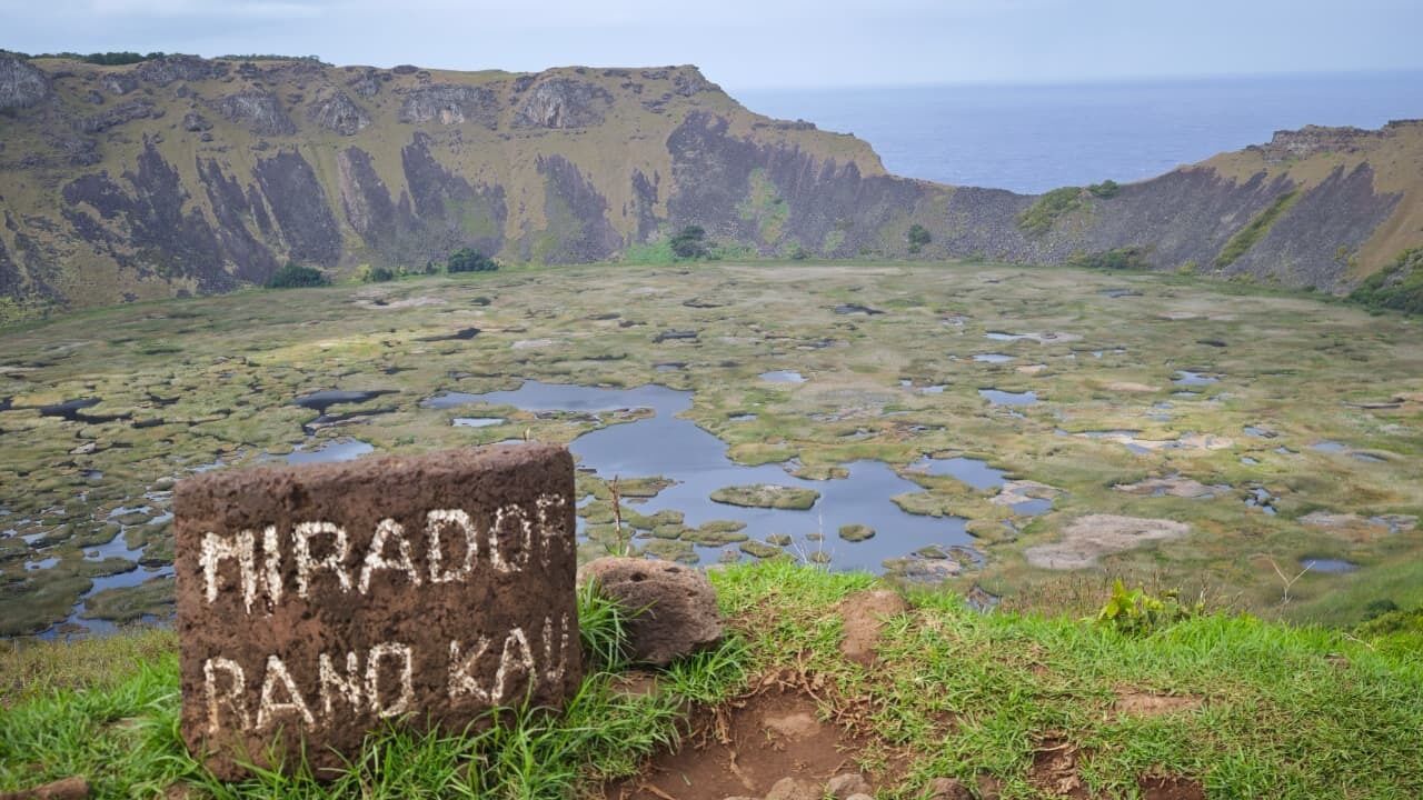 A natural landscape with a rock inscribed with 'Mirado Ranokai' and a view of a coastal area with cliffs and a body of water.