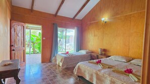 Een kamer met twee bedden, een houten plafond, een betegelde vloer, een tafel en uitzicht op groen.