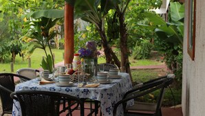 An outdoor dining area with a table set for two, surrounded by lush greenery and a banana tree.