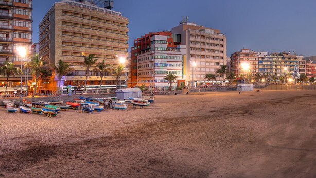 Un paysage urbain au bord de la mer, avec une plage de sable, des bateaux et des bâtiments.