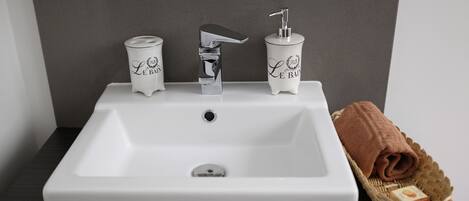 Uma pia de banheiro branca com uma torneira moderna e dois dispensadores de sabonete rotulados "Le Bain".