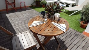 Une terrasse en bois avec une table ronde dressée pour le repas, entourée de plantes en pot et de mobilier d’extérieur.