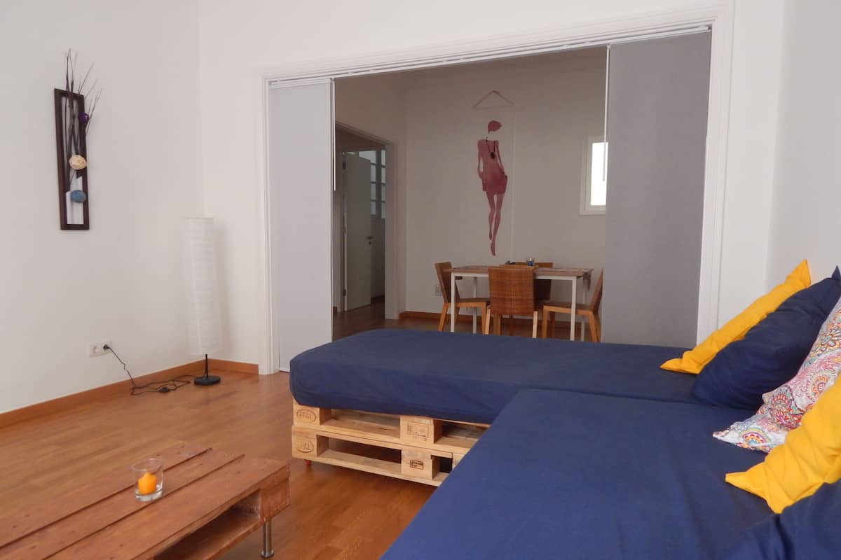 Een slaapkamer met een bed, een nachtkastje van hout en een klein tafeltje met een kaars.