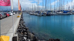 Un port de plaisance où de nombreux voiliers sont amarrés le long d’une promenade en bord de mer, une rangée de drapeaux et un ciel bleu azur.