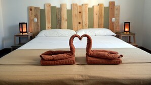 Un lit avec une tête de lit en bois, deux tables de chevet avec des lampes, et deux serviettes disposées en forme de cœur sur le lit.