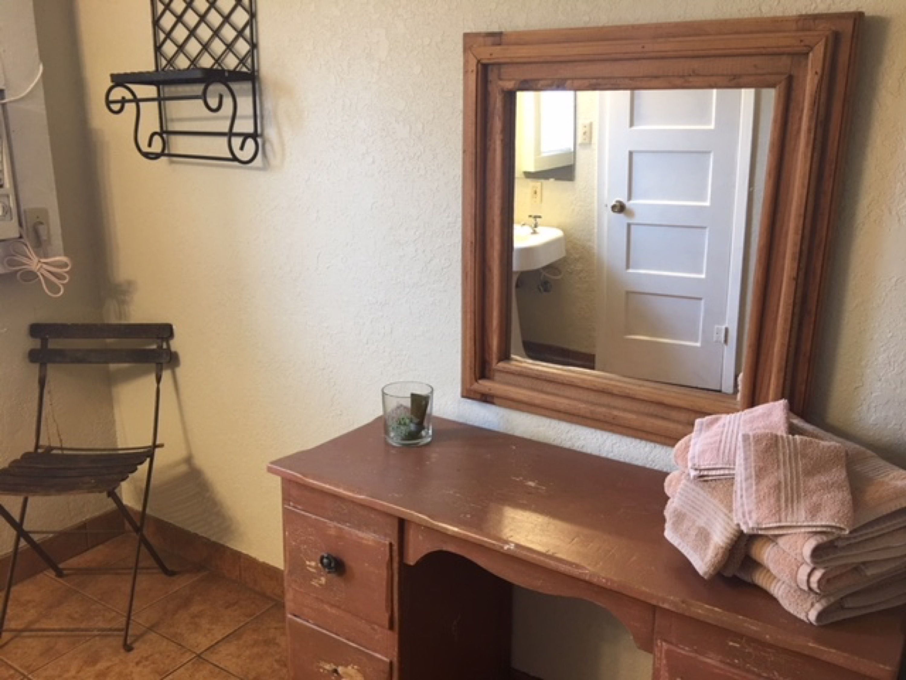 A wooden dresser with a mirror, a small glass container, and a chair.