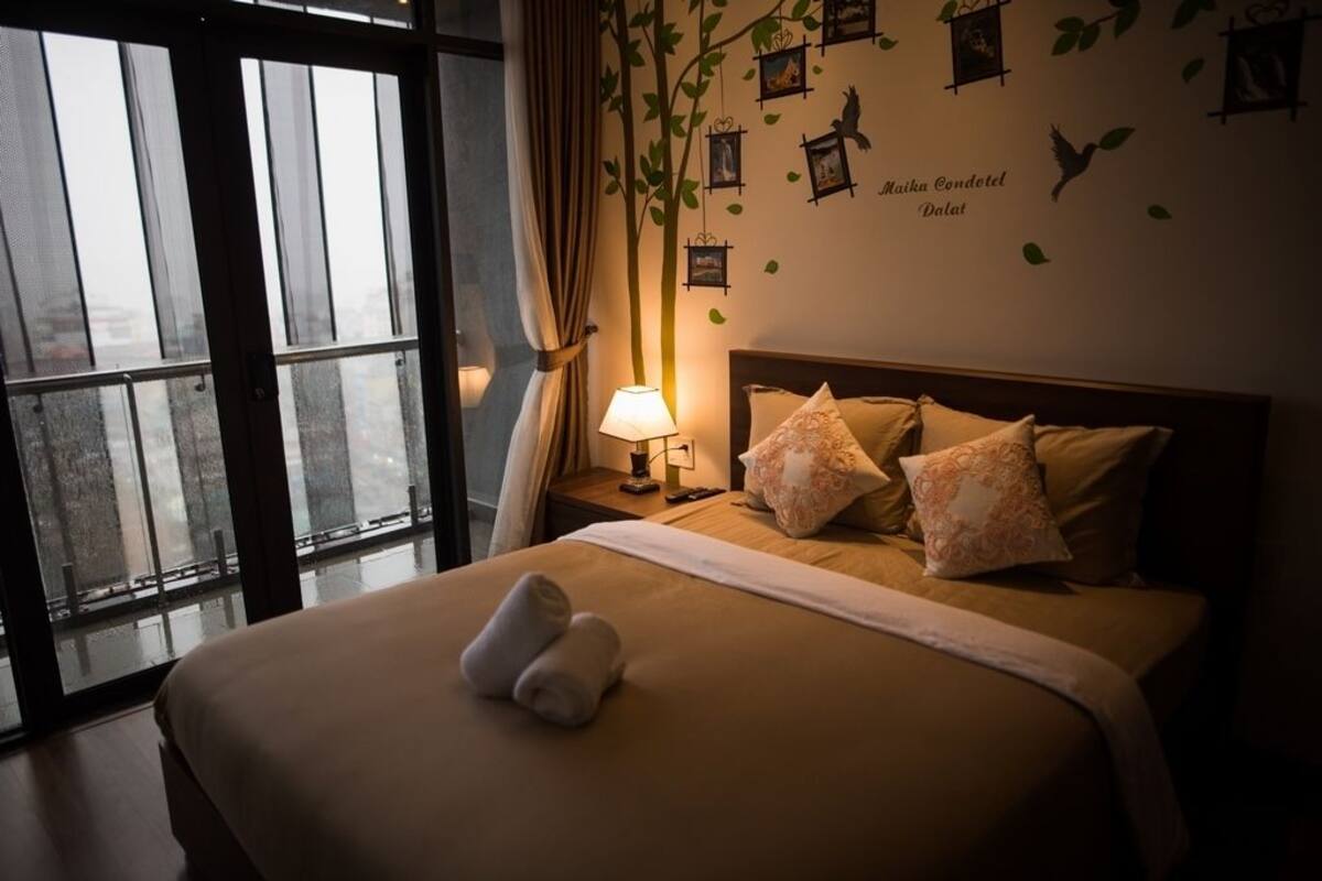 Una habitación de hotel con una cama grande, una mesita de noche con lámpara y una ventana con cortinas.