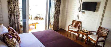 A hotel room with a bed, two wooden chairs, a TV mounted on the wall, and a view of the outside balcony.