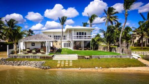 Ein zweistöckiges Haus mit Pool, umgeben von Palmen und einem Strand.