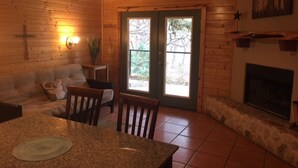 L’intérieur chaleureux d’un chalet avec un plancher en bois, une cheminée en pierre, une table à manger avec des chaises, un canapé et une croix accrochée au mur.