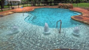 Une piscine à l’eau claire, avec une échelle et un élément décoratif en pierre au centre.