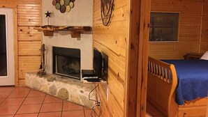 Une pièce chaleureuse dans un chalet en rondins, avec une cheminée, un lit et un manteau de cheminée en pierre.