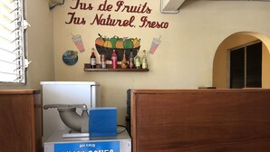 Un distributeur de boissons sur lequel est apposée une pancarte indiquant « Boissons glacées, rafraîchissantes et désaltérantes » et un mur orné d’une affiche qui dit « Jus de fruits, entièrement naturels, Fresca », avec des images de fruits et de boissons.