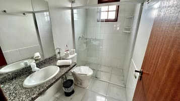 A bathroom with a granite countertop, two sinks, a toilet, a shower, and a mirror.